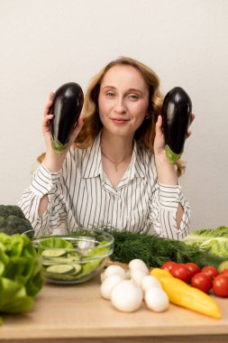 Masada elinde patlıcan olan bir kadın. Masada taze sebzeler var. Vejetaryen yemeği. Yüksek kalite fotoğraf