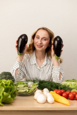 Masada elinde patlıcan olan bir kadın. Masada taze sebzeler var. Vejetaryen yemeği. Yüksek kalite fotoğraf