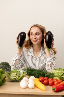Masada elinde patlıcan olan bir kadın. Masada taze sebzeler var. Vejetaryen yemeği. Yüksek kalite fotoğraf