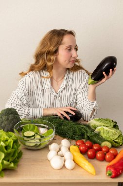 Masada elinde patlıcan olan bir kadın. Masada taze sebzeler var. Vejetaryen yemeği. Yüksek kalite fotoğraf
