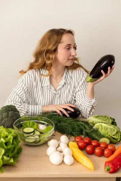 Masada elinde patlıcan olan bir kadın. Masada taze sebzeler var. Vejetaryen yemeği. Yüksek kalite fotoğraf