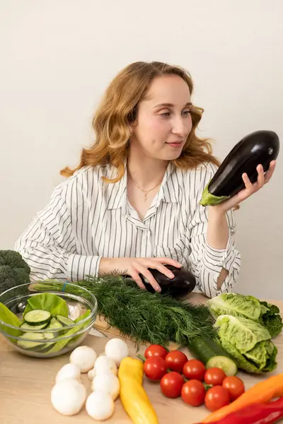 Masada elinde patlıcan olan bir kadın. Masada taze sebzeler var. Vejetaryen yemeği. Yüksek kalite fotoğraf