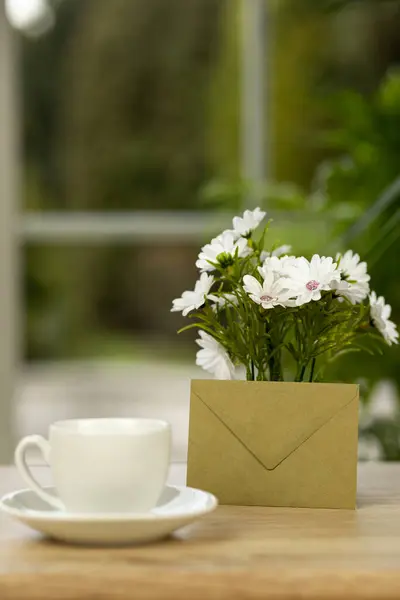 Bir fincan kahve, çiçekler ve bir zarf. Ofis masasında bir fincan kahve. Pencerenin yanındaki masaüstü. Yüksek kalite fotoğraf