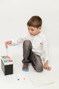 Çocuk keçeli kalemi paketten çıkarır. Beyaz arka planda işaretleri olan bir çocuk. Yüksek kalite fotoğraf