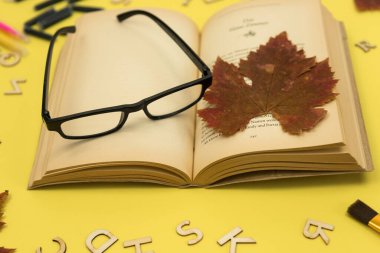 Sarı arka planda gözlüklü açık bir kitap. Sonbahar eğitimi ile ilişkili. Okulda, üniversitede eğitim. Kitap okuyorum. Yüksek kalite fotoğraf
