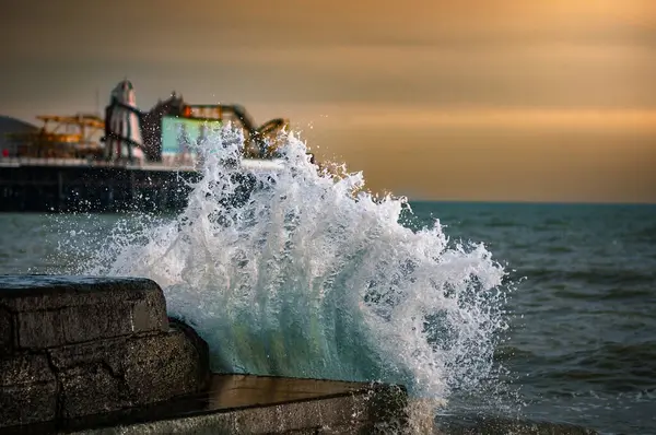 Brighton, Doğu Sussex, İngiltere 'de rüzgarlı bir akşamda büyük bir dalga iskelenin taş duvarına çarpıyor..