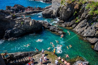 Kayalık sahilin güzel manzarası ve deniz kıyısında dinlenen insanlar, Manarola köyü, İtalya