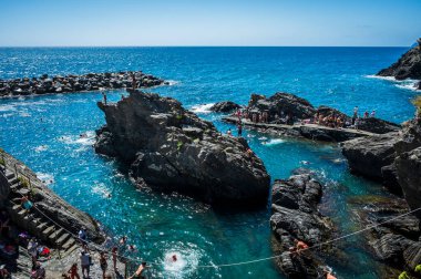 Kayalık sahilin güzel manzarası ve deniz kıyısında dinlenen insanlar, Manarola köyü, İtalya