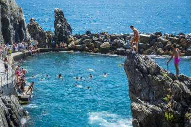 Kayalık sahilin güzel manzarası ve deniz kıyısında dinlenen insanlar, Manarola köyü, İtalya
