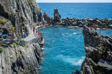 Kayalık sahilin güzel manzarası ve deniz kıyısında dinlenen insanlar, Manarola köyü, İtalya
