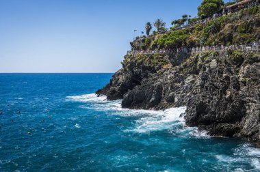 Kayalık sahilin güzel manzarası ve deniz kıyısında dinlenen insanlar, Manarola köyü, İtalya
