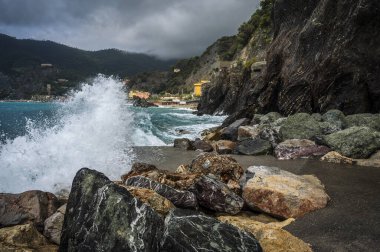 Dalgalar kayalık deniz kıyısına çarpıyor. Cinque Terre 'de. Monterosso, liman, sahil ve antik köy.                                  