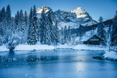 Göldeki eski kulübe. Kış dağlarında ormanla çevrili. 