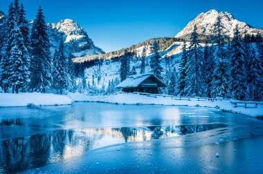 Göl kenarındaki ahşap kulübe kışın dağlarda karla kaplı ağaçlarla çevrili. 