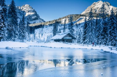Göl kenarındaki ahşap kulübe kışın dağlarda karla kaplı ağaçlarla çevrili. 