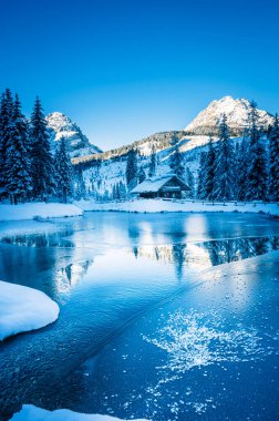 Göl kenarındaki ahşap kulübe kışın dağlarda karla kaplı ağaçlarla çevrili. 