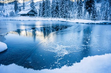 Göl kenarındaki küçük ahşap kulübe. Kış dağlarında ağaçlarla çevrili. 