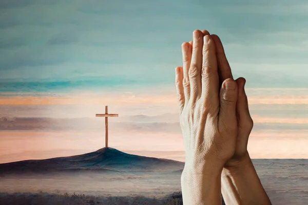 Hands in pray against Easter cross and sunset landscape. Copy space. Shining cross on Calvary hill, sunrise sky background. Faith in Jesus Christ. Christianity. Church worship, salvation concept.