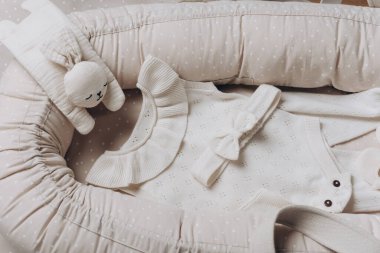 Bebek takımları, kız şamatası, tozluklar, aksesuarlar, baş yayı, botlar, bej kozanın üstündeki tavşan oyuncağı, yuva arka planı. Moda, yeni doğan esasları, ıvır zıvır ve aksesuarlar. Üst görünüm.