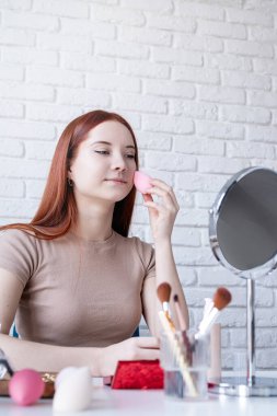 young beautiful woman holding make-up brushes and making up with cosmetics set at home