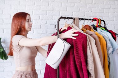 beautiful young woman in trendy outfit standing in front of hanger rack and choosing outfit dressing. Selection of a wardrobe, stylist, shopping. Clothes designing