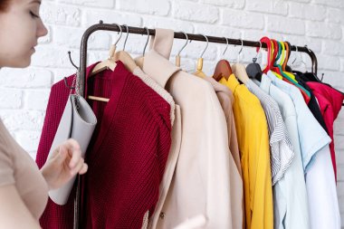 beautiful young woman in trendy outfit standing in front of hanger rack and choosing outfit dressing. Selection of a wardrobe, stylist, shopping. Clothes designing