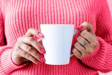 viva magenta color of the year 2023. closeup woman hands in sweater holding white mug for mockup design toned with viva magenta