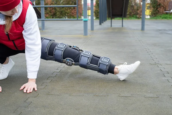 Woman wearing knee brace or orthosis after leg surgery working out in the park . Medical and healthcare concept.