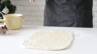 Selective focus of male chef making cinnamon rolls, christmas tree with lights on the background, festive cooking