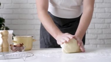 Selective focus of male chef making cinnamon rolls, christmas tree with lights on the background, festive cooking
