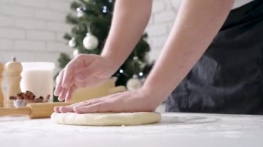 Selective focus of male chef making cinnamon rolls, christmas tree with lights on the background, festive cooking