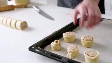 Selective focus of male chef making cinnamon rolls, christmas tree with lights on the background, festive cooking