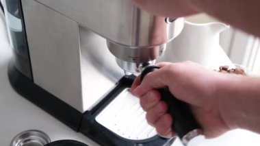 male hands holding portafilter and making fresh aromatic coffee at home using a modern coffee maker