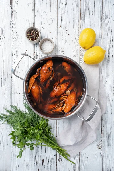 cooked crawfish in saucepan with pickle water with lemons and spices on wooden background