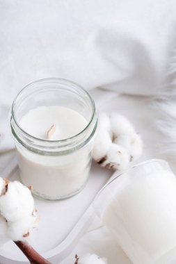 Beyaz kavanozdaki soya aromalı mum ve pamuk dalı. Mum modelleme tasarımı. Doğal olarak balmumu mumunu taklit et..
