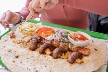 Fast food sokak kafesinde tepside pide ekmekli ve sebzeli ızgara kebap yiyen bir kadın. Taze sebze ve et çukurunda shawarma. Ulusal Ermeni yemekleri