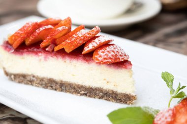 Gerçek kafe masasında meyveli bir parça lezzetli cheesecake. Arka planda bir fincan kahve.