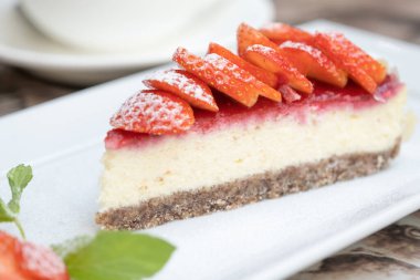 Gerçek kafe masasında meyveli bir parça lezzetli cheesecake. Arka planda bir fincan kahve.
