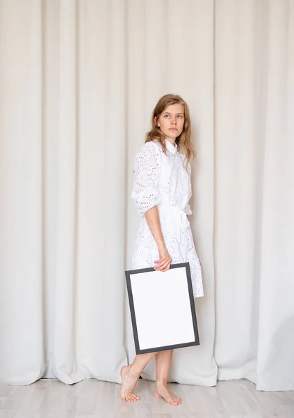 光着脚的女人 穿着漂亮的白色衣服 手握无框 米色窗帘背景 造型设计 — 图库照片