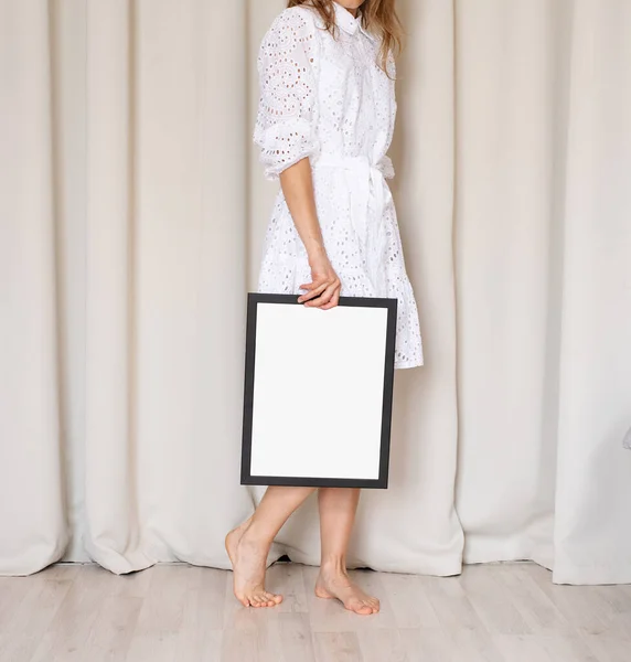 穿着漂亮的白色衣服 手持空白框架 米色窗帘背景 造型图案的赤脚女子 — 图库照片