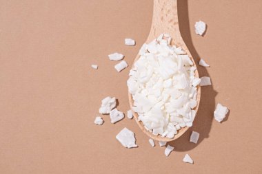 Ev yapımı beyaz soya mumları için soya mumu. Kahverengi arka planda tahta kaşıkta soya mumunun yakın plan görüntüsü, boşluğu kopyala