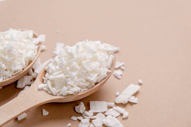 Ev yapımı beyaz soya mumları için soya mumu. Kahverengi arka planda tahta kaşıkta soya mumunun yakın plan görüntüsü, boşluğu kopyala