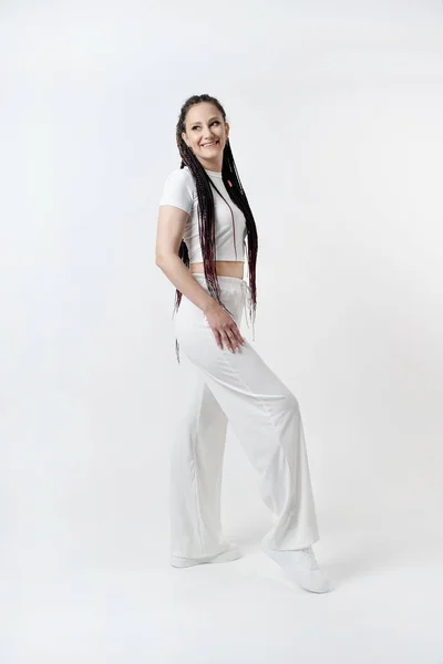 stock image Fashionable young beautiful woman . Slim girl with dreadlocks in an active pose in a white pants and top . Fashion, clothing and style.