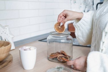 Mutlu Noeller ve mutlu yıllar. Kadın elleri, Noel 'e hazırlanmak için cam kabın içine kuru narenciye parçaları koyuyor. Yiyecek korunumu
