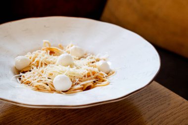 Kafedeki ahşap masada mozarella topları ve domates soslu lezzetli vejetaryen makarna.