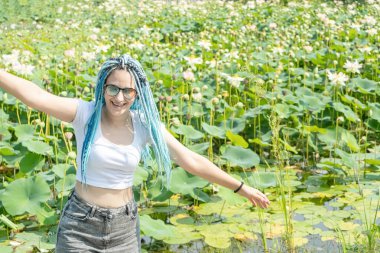 Mavi afro kilitleri olan genç ve güzel bir kadın lotus gölünde dinleniyor doğanın tadını çıkarıyor.