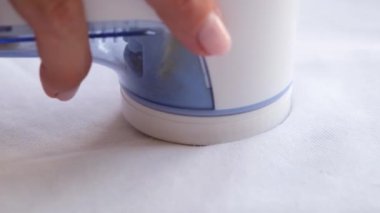 Kadınlar beyaz kazaktaki kumaş ve giysilerdeki pelet ve makaraları çıkarmak için makine kullanırlar. Eski şeyleri güncellemek için modern bir elektronik cihaz.