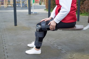 Woman wearing sport clothes and knee brace or orthosis after leg surgery, walking down the stairs in the park. Medical and healthcare concept.