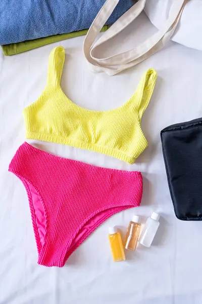 Vacation concept. Travel cosmetics kit an bathing suit on bed , top view