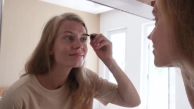 Otel odasında aynanın karşısında kaşlarını fırçalayan güzel bir kadın.